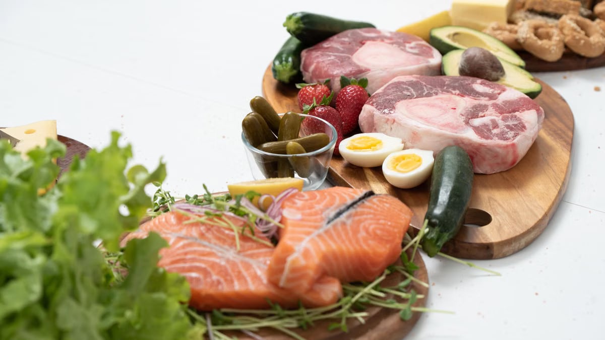 Assorted fresh keto ingredients including salmon, beef, and vegetables on wooden boards, perfect for healthy meals.